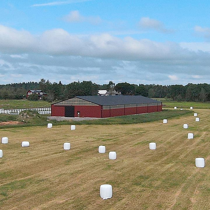 Åkermark med rött ridhus i bakgrunden